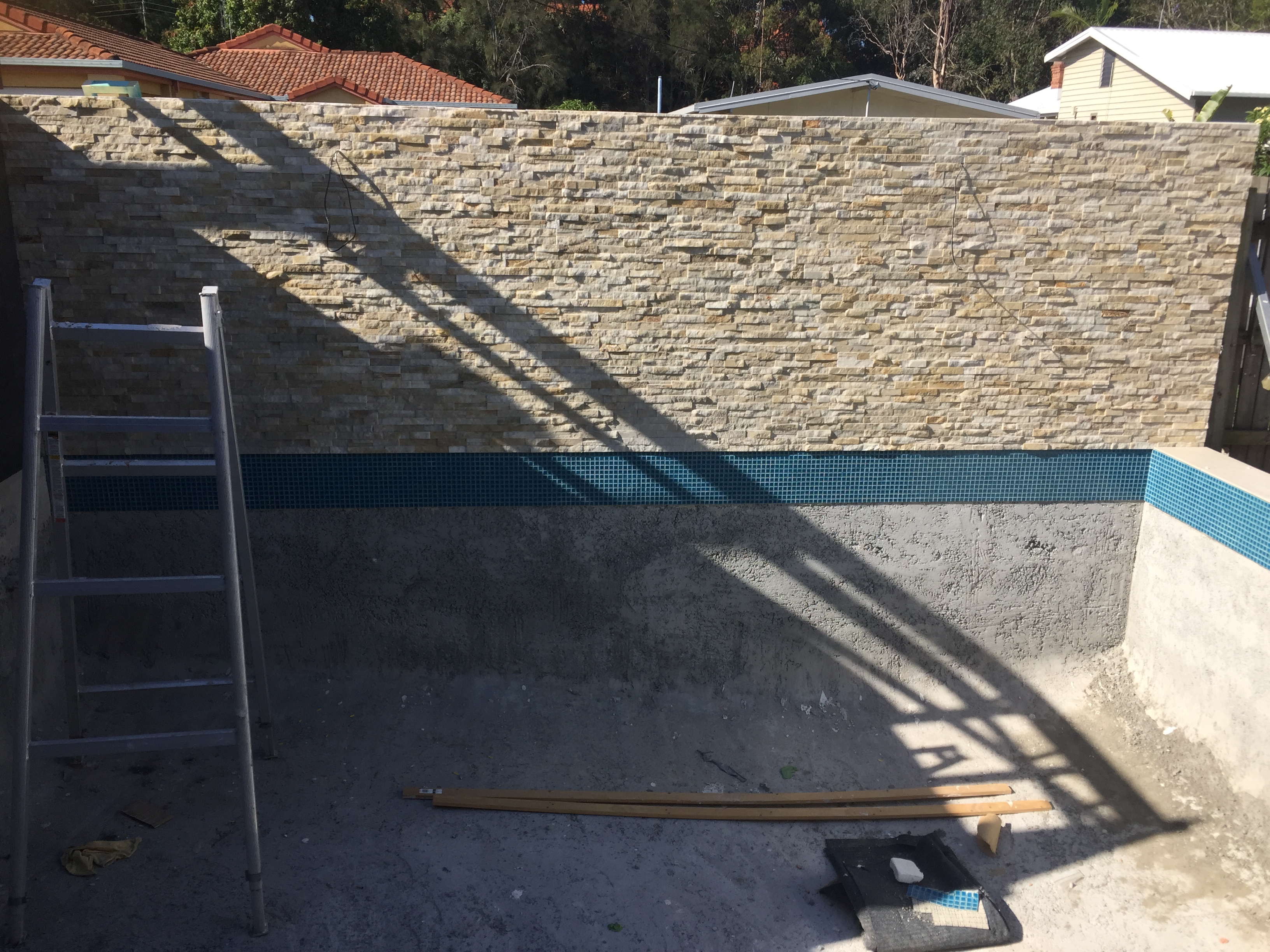 New pool shell with stacked stone feature wall and mosaic tile waterline during construction at Gold Coast renovation