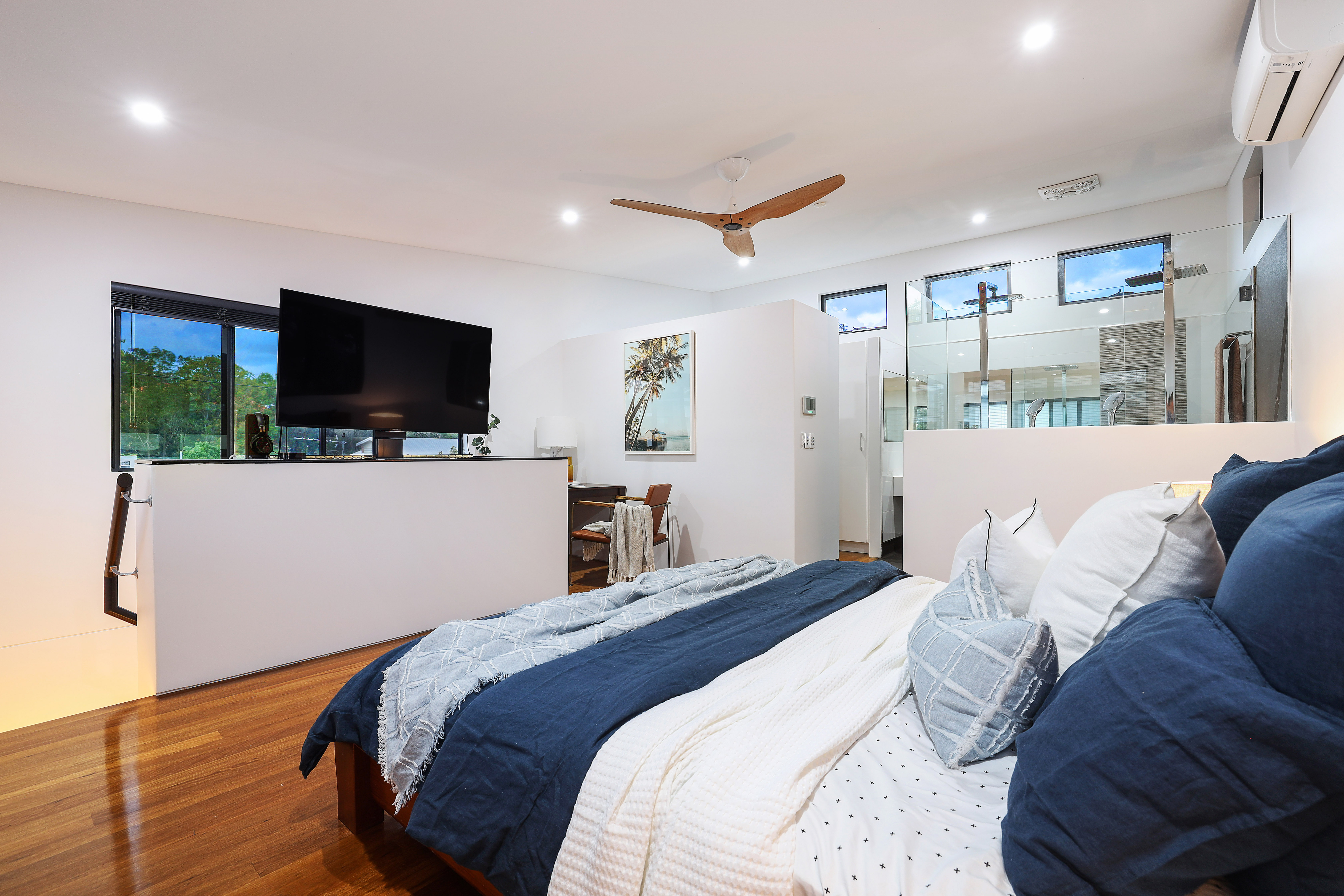 Upstairs master bedroom with ensuite visible through glass partition, timber ceiling fan and polished floors at renovated Southport home