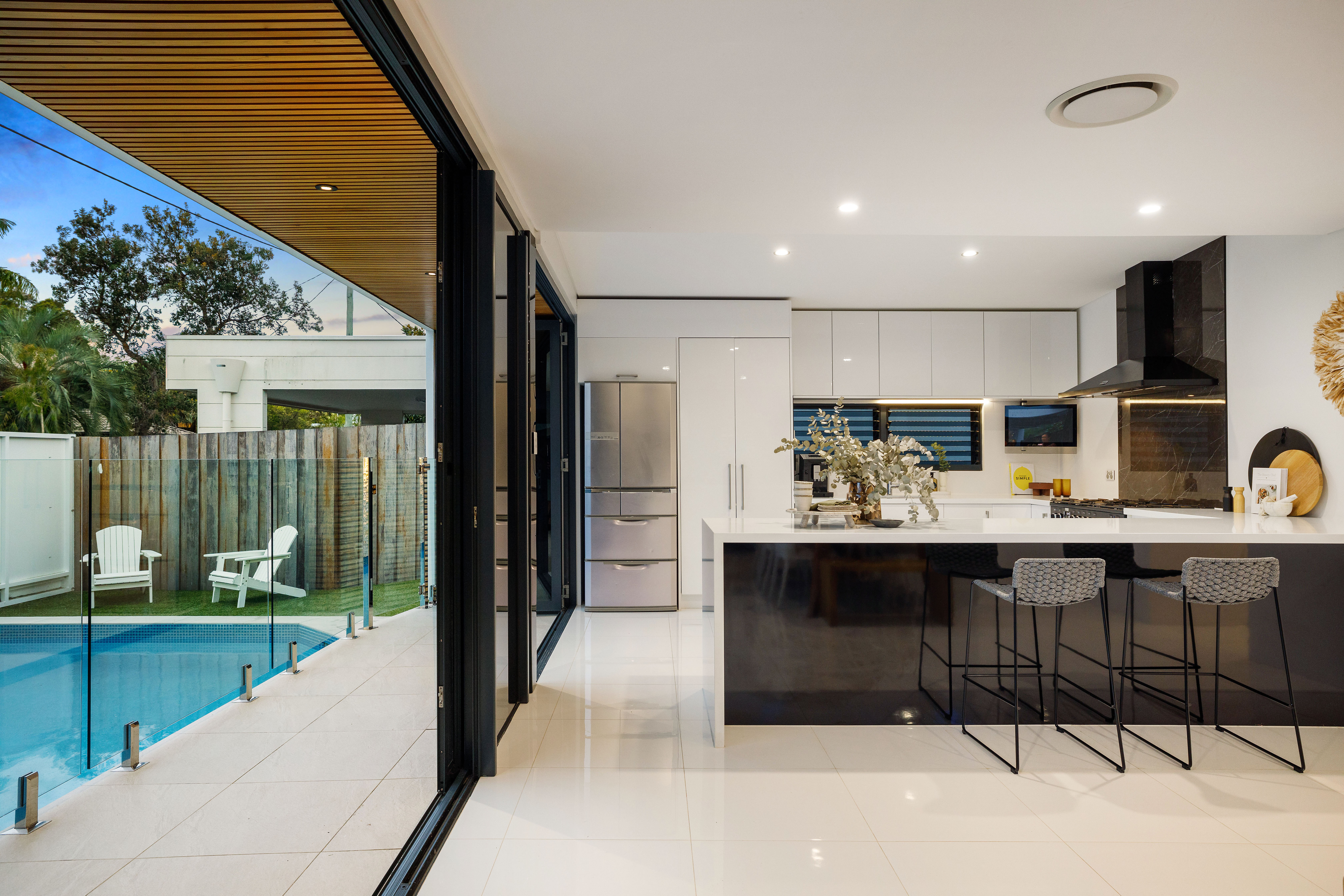 Modern kitchen with dark island bench and bar stools, bifold doors open to saltwater pool at completed Southport Gold Coast renovation