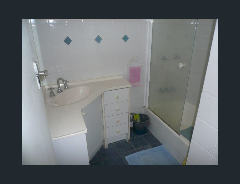 Small dated bathroom with blue accent tiles, cramped vanity and shower screen before Gold Coast renovation