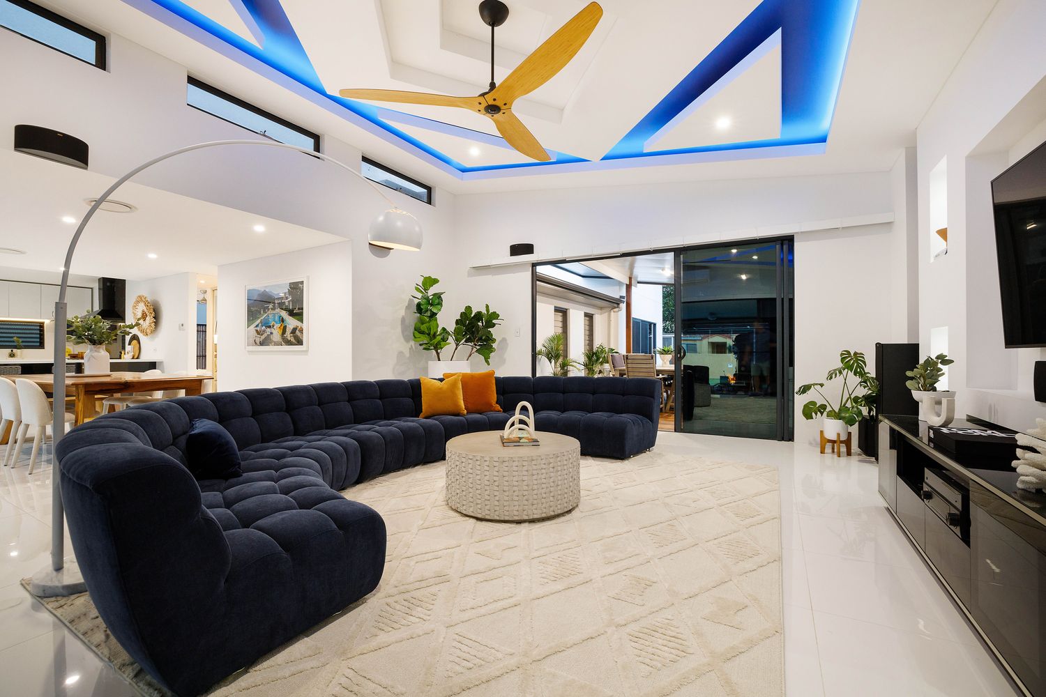 Spacious living room with navy modular sectional, blue LED recessed ceiling lighting and open plan to dining at renovated Southport home